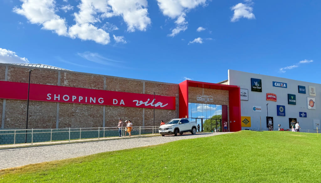 Fachada do Shopping da Vila, com o letreiro vermelho sobre os tijolos históricos e as lojas ao lado